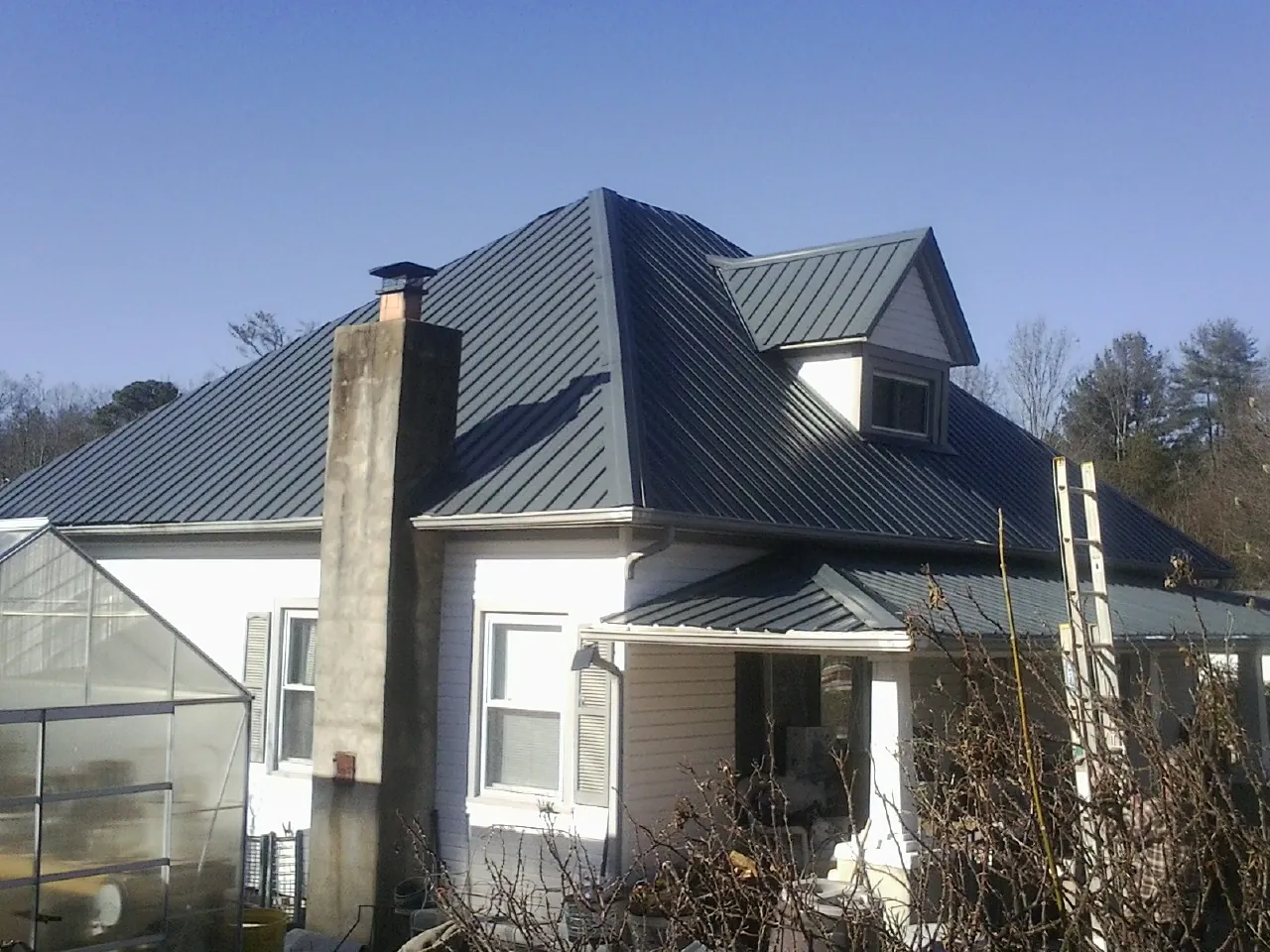 Dark blue standing seam metal roof on a white farmhouse with dormer — Slate & Tile Roof Repair by Roofing Brothers in Stantonville