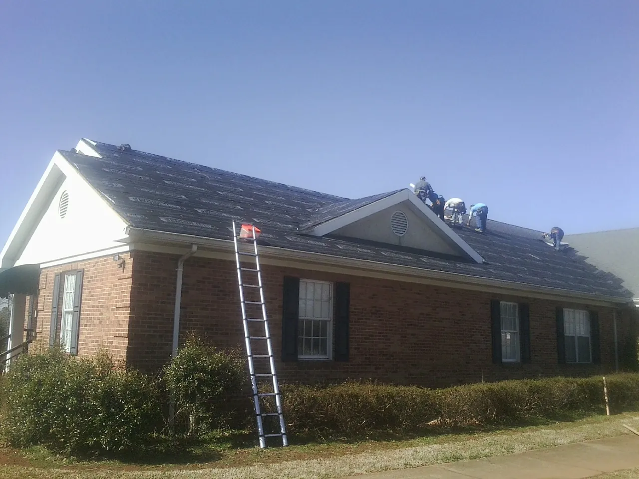 Crew tearing shingles off a brick ranch roof with a ladder set — Metal Roof Repair work by our crew in Stantonville