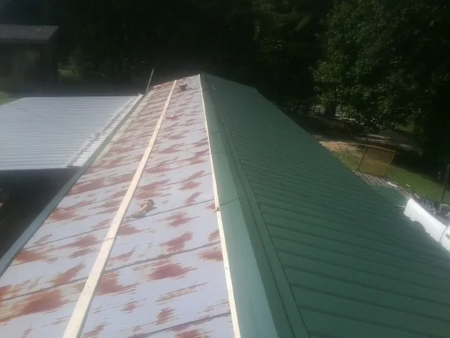 Old rusted panels beside newly installed green metal roofing — Wind Damage Roof Repair by Roofing Brothers in Stantonville