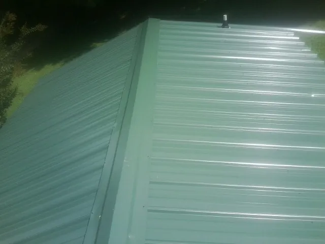 New green metal panels meeting at the ridge of a roof — Flat Roof Repair work by our crew in Stantonville