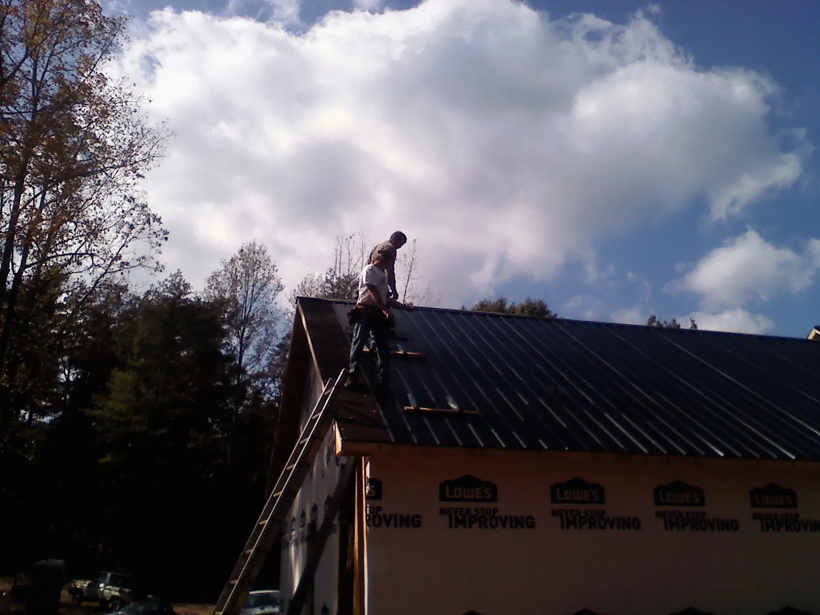 Roofer fastening dark metal panels high against a cloudy sky, from a Roof Inspection job in Stantonville