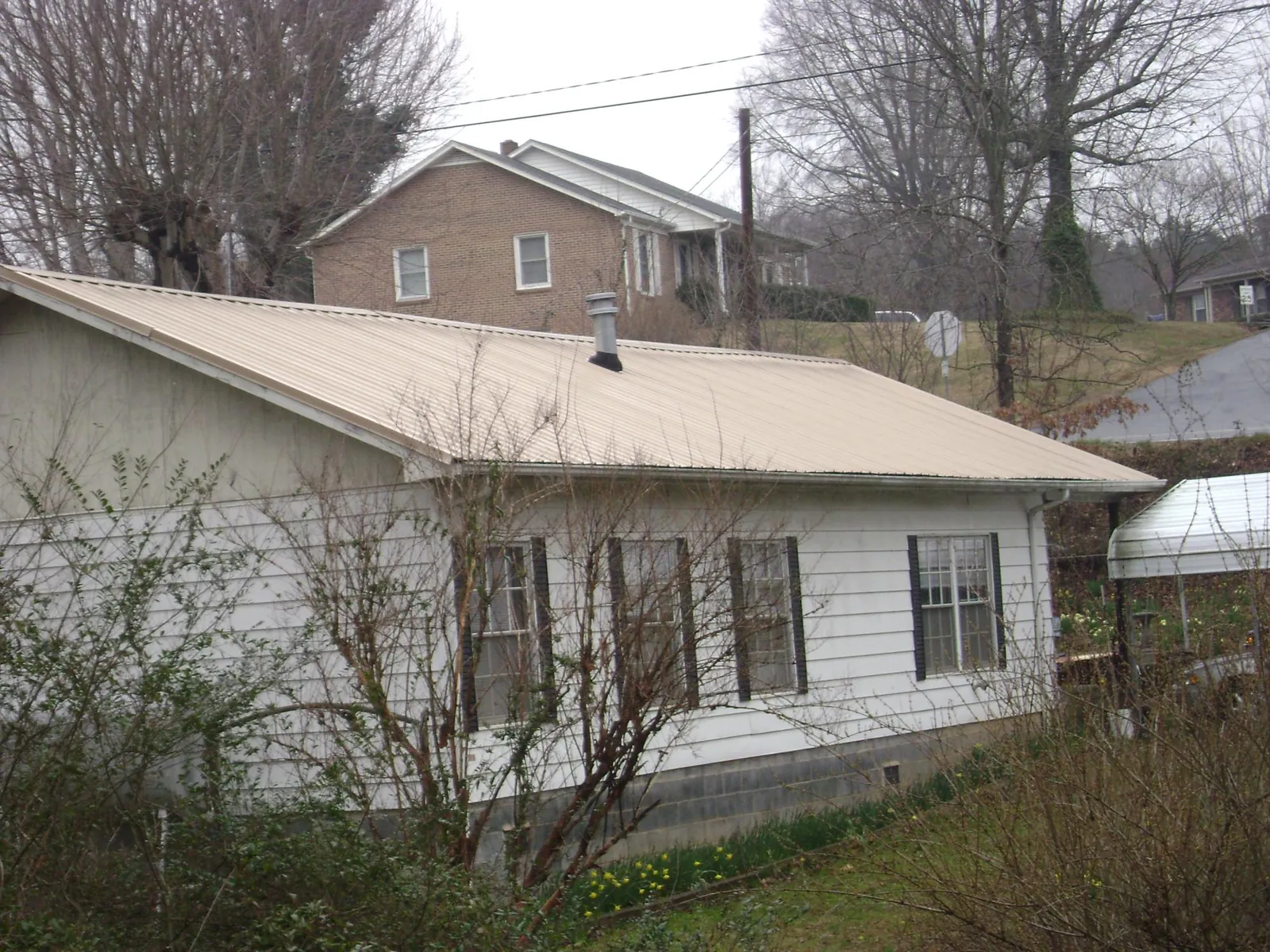 Tan metal roof on a white sided house set into a hillside — Commercial Roofing by Roofing Brothers in Stantonville